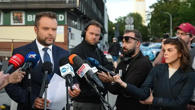 Rzecznik PiS przemawia na konferencji prasowej. Obok dziennikarze i mikrofony