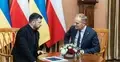 Wołodymyr Zełenski i Donald Tusk rozmawiają przy stole. W tle flagi Polski i Ukrainy