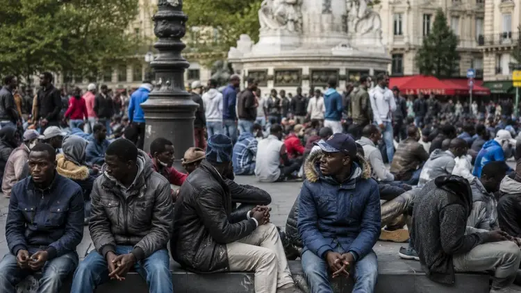 Migranci siedzący na placu w Paryżu