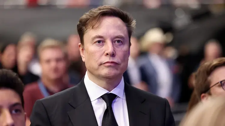 Elon Musk w garniturze, w tle i obok niego ludzie