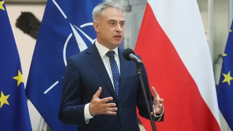 Krzysztof Gawkowski przemawia i gestykuluje. W tle flaga Polski, UE i NATO
