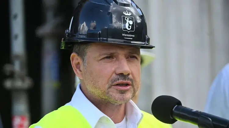 Rafał Trzaskowski w kasku i żółtej kamizelce przemawia do mikrofonu