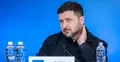 Wołodymyr Zełenski drapie się po szyi. Niebieskie tło, na stole stoi woda
