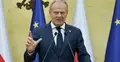 Donald Tusk przemawia do mikrofonu i gestykuluje na konferencji prasowej. W tle flaga Polski i UE