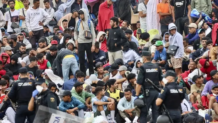 Migranci pilnowani przez policję na plaży w Ceucie