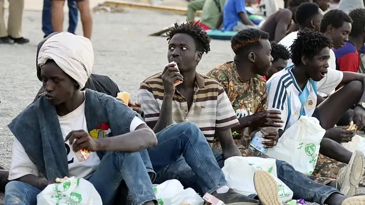 Migranci siedzący na plaży w Ceucie