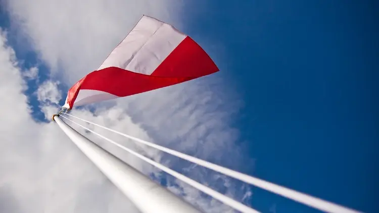 Polska flaga na maszcie na tle nieba