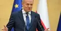 Donald Tusk przemawia do mikrofonu i gestykuluje. W tle flaga Polski i UE