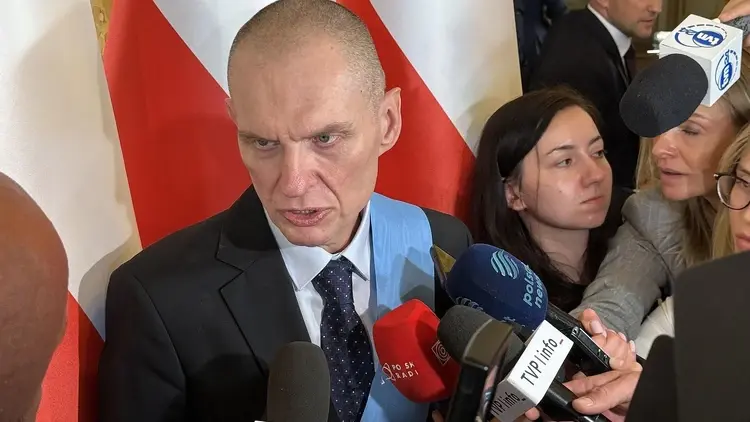 Andrzej Poczobut mówi do dziennikarzy na konferencji prasowej. W tle polskie flagi