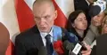 Andrzej Poczobut mówi do dziennikarzy na konferencji prasowej. W tle polskie flagi