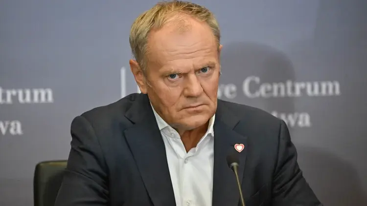 Donald Tusk siedzi przy stole, obok mikrofon