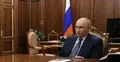 Władimir Putin siedzi przy stole z dłonią na biurku, w tle flaga Rosji