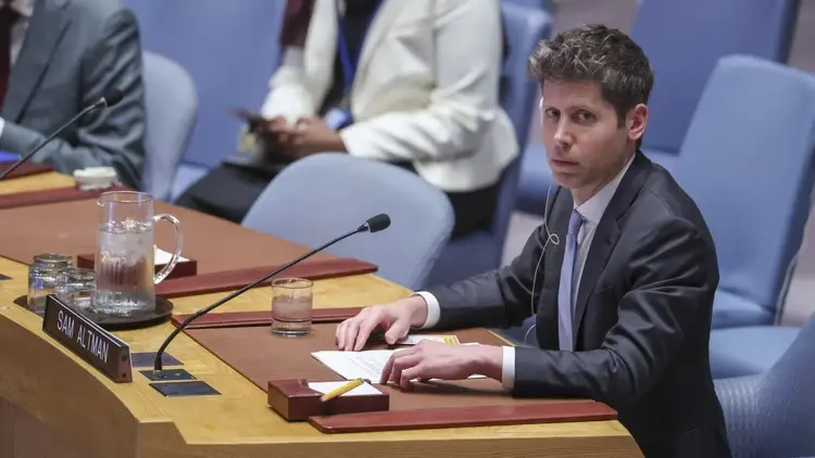 Sam Altman siedzi w garniturze i przemawia do mikrofonu, w tle krzesła i ludzie