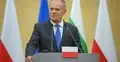 Donald Tusk przemawia, w tle flagi Polski