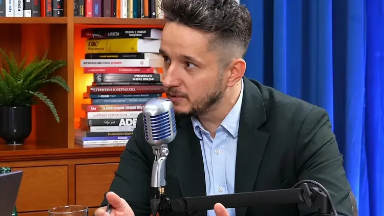 Jakub Wiech mówi do mikrofonu, w tle biblioteczka i niebieska kotara