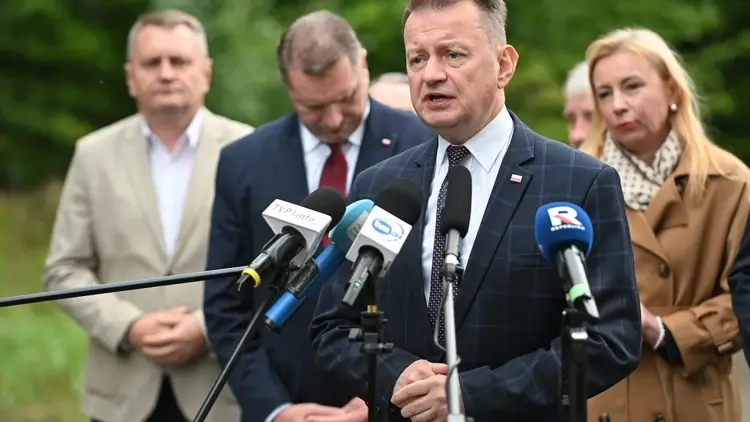 Mariusz Błaszczak przemawia do mikrofonu na konferencji prasowej. W tle ludzie