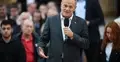 Premier Donald Tusk przemawia do mikrofonu na stojąco. W tle ludzie