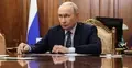 Władimir Putin siedzi przy stole. W tle flaga Rosji
