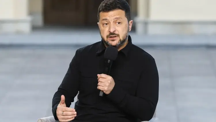 Wołodymyr Zełenski siedzi na krześle na placu i przemawia do mikrofonu