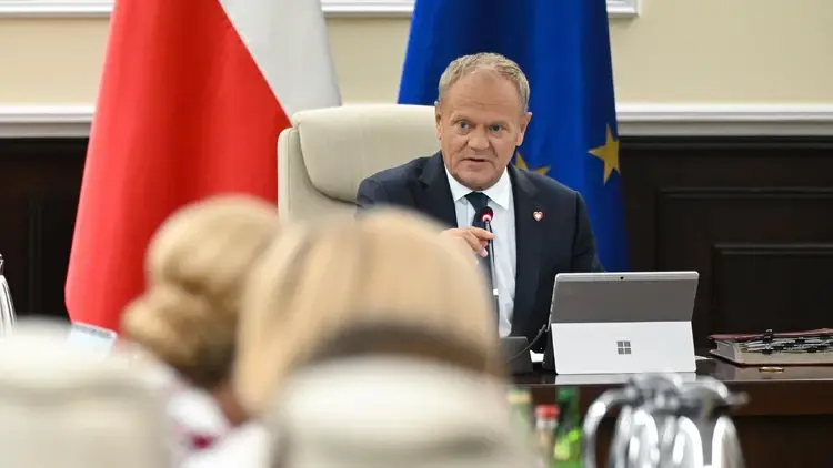 Donald Tusk siedzi przy stole, w tle flaga Polski i UE
