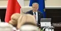 Donald Tusk siedzi przy stole, w tle flaga Polski i UE